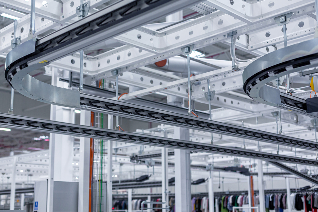 Garments on hangers are being moved by clip and pin conveyors