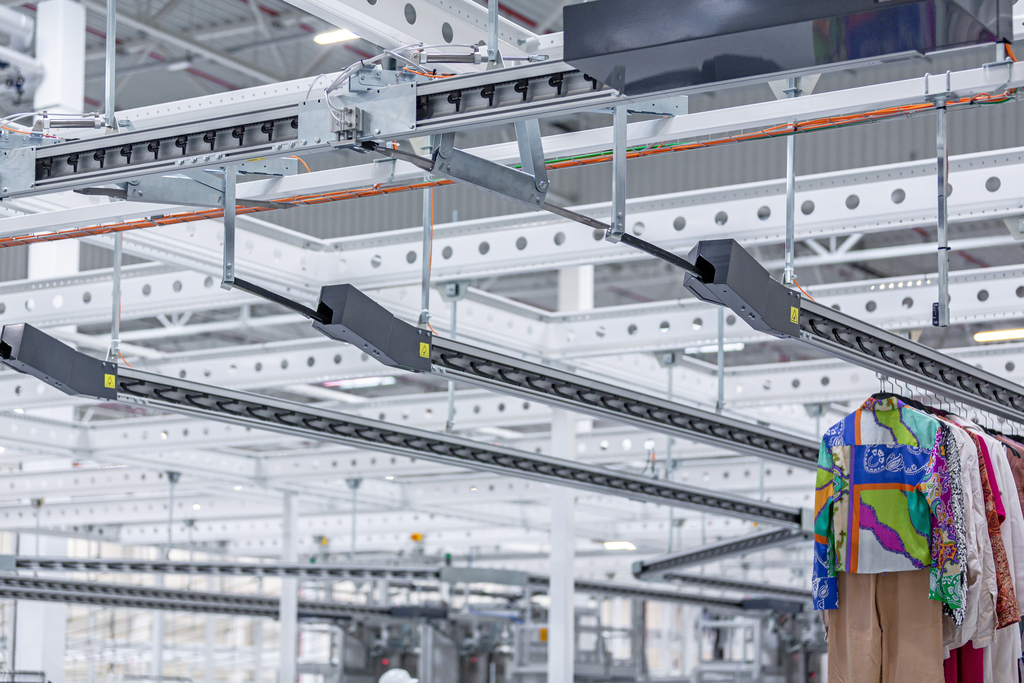 The garments on hangers are being moved garment conveyors inside the warehouse