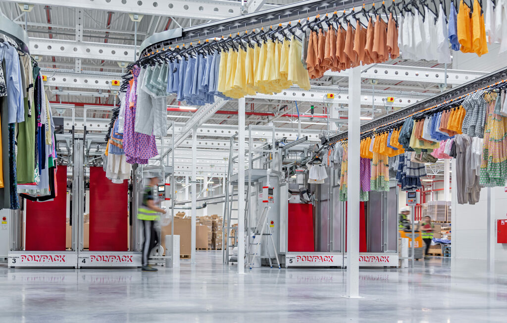 Automated garment clip conveyor system moving clothes on hangers toward an industrial bagging machine in a dry cleaning or laundry facility.